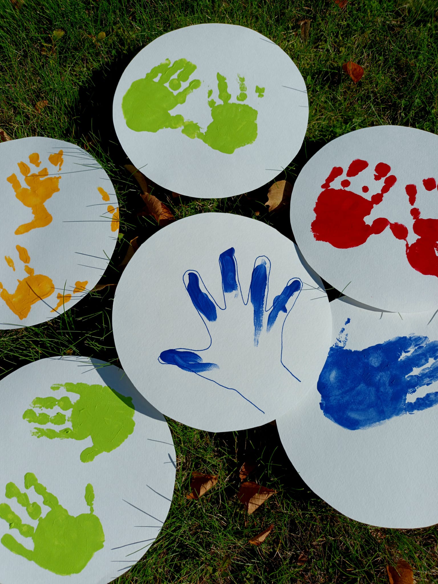 Lasten ja aikuisten eri värisiä painettuja käden kuvia valkoisissa ympyröissä ruohikolla.