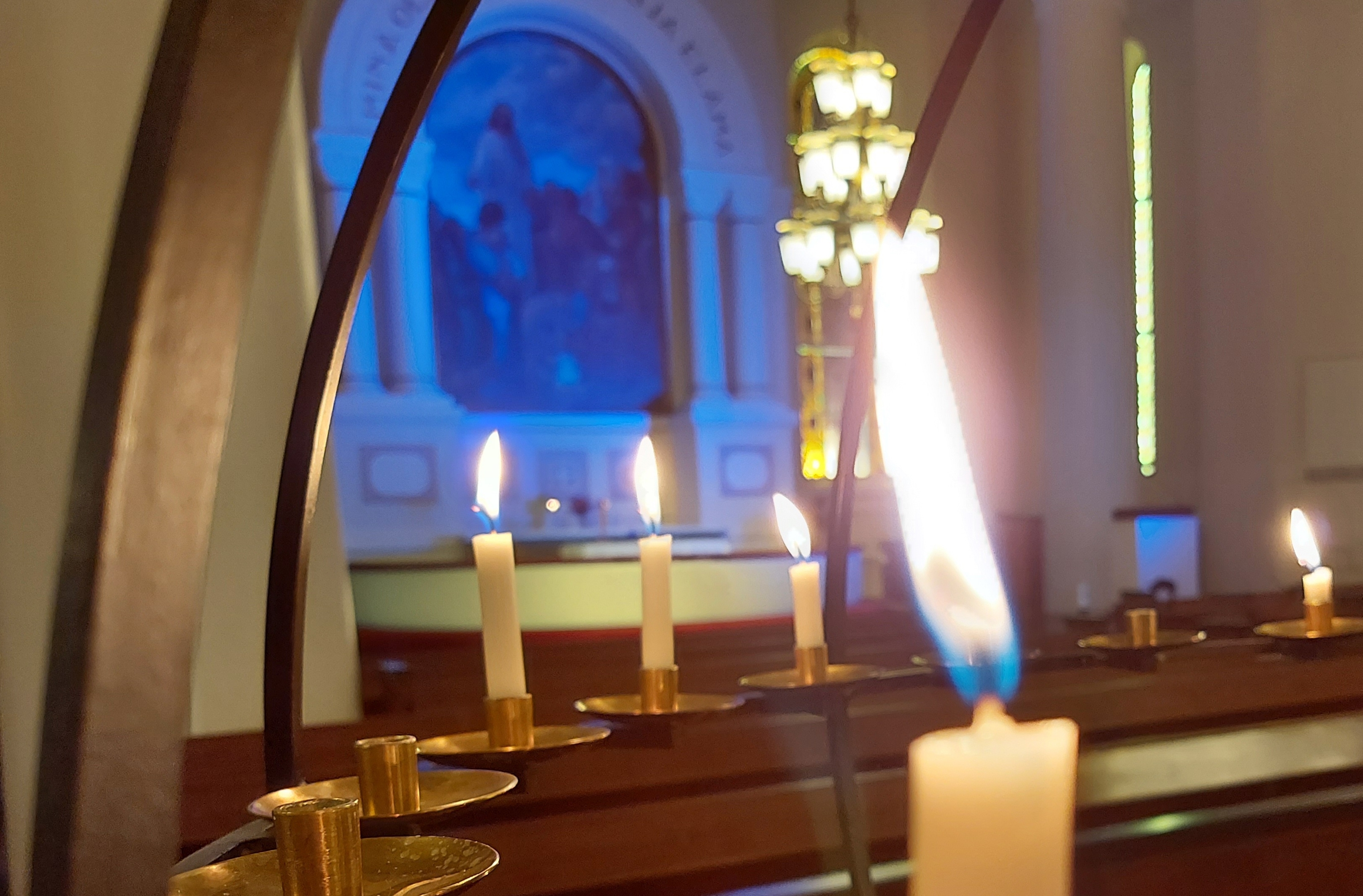 lähikuva Lopen kirkon lähetyskynttelikössä palavasta kynttilästä. Taustalla alttari joka on valaistu Ukrain...